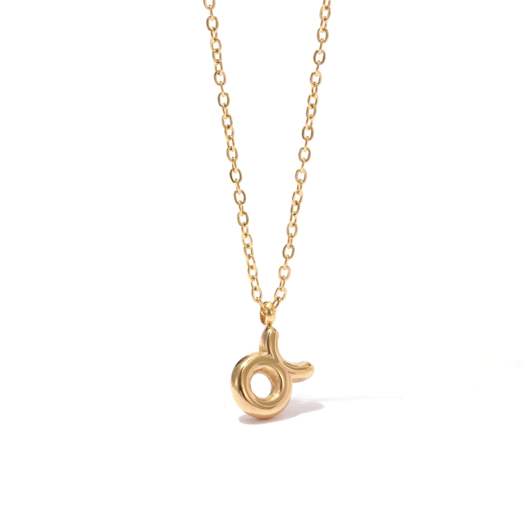 All 12 zodiac symbol bubble necklaces in 18K gold PVD displayed on a stone surface. Bold, chunky glyph pendants on delicate cable chains — waterproof and tarnish-free.