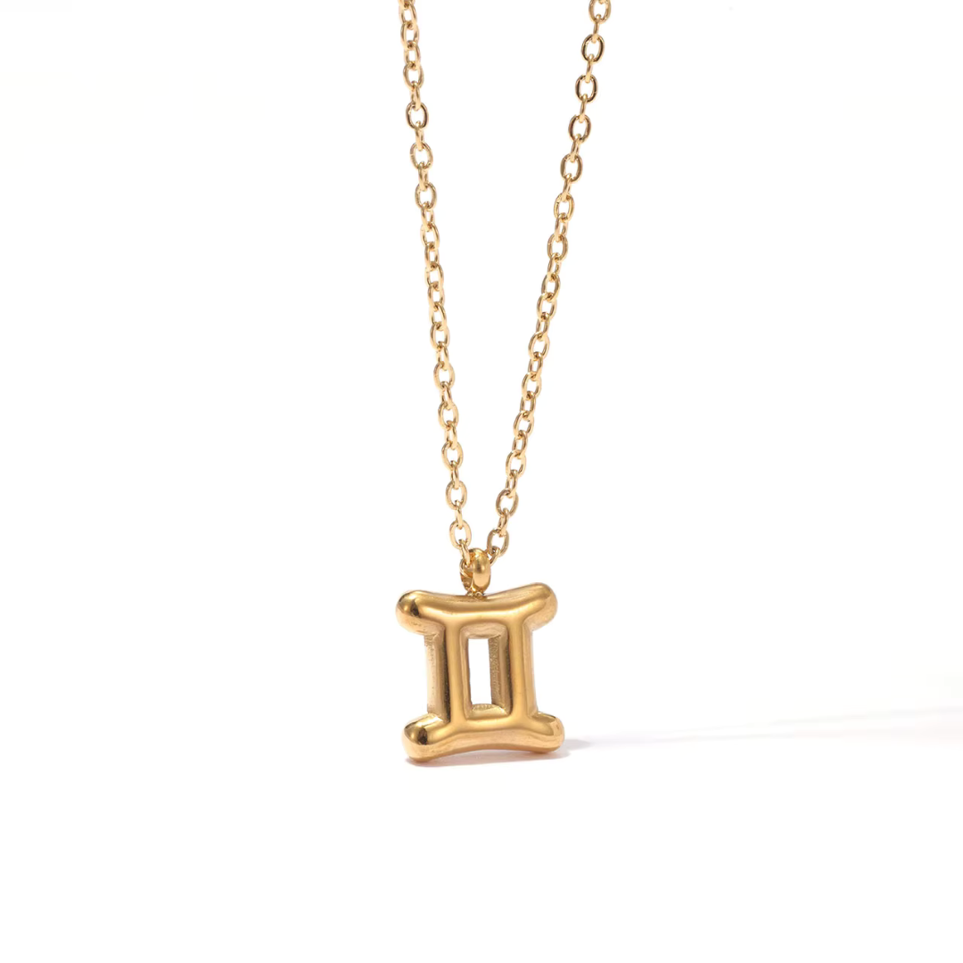 All 12 zodiac symbol bubble necklaces in 18K gold PVD displayed on a stone surface. Bold, chunky glyph pendants on delicate cable chains — waterproof and tarnish-free.